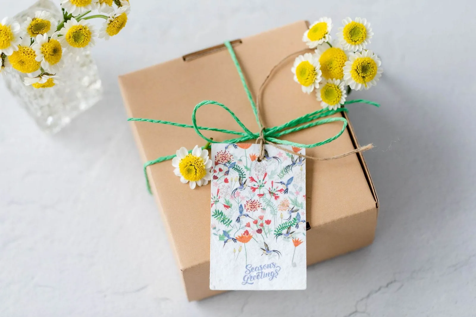 Kraft gift box tied with twine and a seed-paper tag beside yellow flowers
